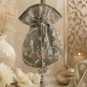 Può includere: Una pochette con coulisse color verde salvia caratterizzata da un intricato ricamo floreale con paillettes, perline e perle multicolori. La borsa presenta un manico in tessuto abbinato e una nappa decorativa alla base della chiusura a coulisse.