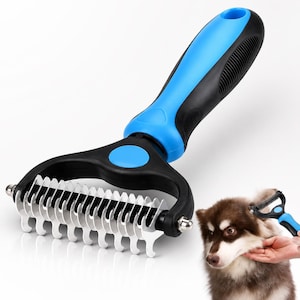 May include: A pet grooming rake featuring a black and blue ergonomic handle with a textured grip. The head consists of a row of curved, stainless steel metal teeth designed for detangling fur, shown in a large view and in use on a brown dog.