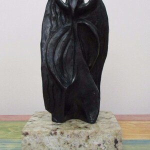 May include: A black, vertically oriented sculpture with an organic, flowing form and a central cutout near the top. The sculpture is mounted on a rectangular, speckled beige and grey granite base with a polished, smooth surface finish.