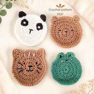 Op de afbeelding: Vier ronde gehaakte onderzetters met dierengezichten: een witte panda, een bruine beer, een lichtbruine kat met snorharen en een groene kikker. De tekst "Crochet pattern PDF" staat boven de onderzetters. Elk item is gemaakt van garen.