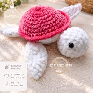 Op de afbeelding: Een gehaakte schildpad knuffel met een felroze schild en een witte kop, flippers en buik. De schildpad heeft zwarte plastic ogen. Tekst op de afbeelding bevat PDF PATTERN, BEGINNER FRIENDLY, STEP-BY-STEP INSTRUCTIONS, INSTANT DOWNLOAD, NO MAGIC RING en Treble Stitch MADE WITH YARN & LOVE.