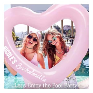 May include: A large, heart-shaped, light pink inflatable pool float with a smooth surface. The text 'NICOLE'S Bachelorette' is printed in white on the left side, and 'Let's Enjoy the Pool Party!' is printed in white at the bottom.