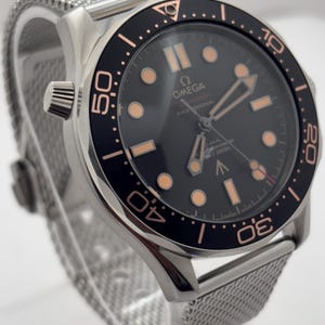 May include: An Omega Seamaster Professional watch with a black dial, luminous hour markers, and a black rotating bezel with copper-toned numerals. The timepiece features a silver-toned stainless steel mesh strap and a metallic watch case.