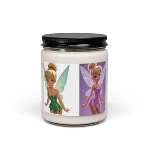 Puede incluir: Una vela blanca en un frasco de vidrio transparente con tapa negra, que presenta una etiqueta con dos ilustraciones de hadas. Un hada viste un vestido verde con alas verde claro, y la otra viste un vestido morado con alas brillantes y translúcidas.