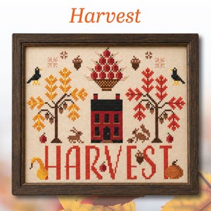 May include: A framed cross-stitch sampler on cream fabric featuring a red house, a basket of red apples, two trees with yellow and red leaves, two black birds, a rabbit, a squirrel, acorns, and the word HARVEST in large red capital letters.