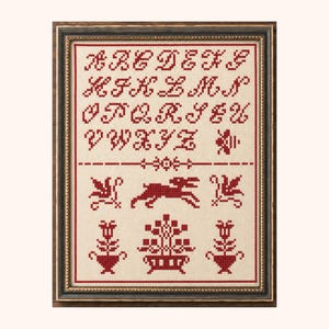 Peut inclure: Un cadre contenant une broderie au point de croix représentant l'alphabet rouge de A à Z sur un tissu beige clair. Sous les lettres, le motif comprend une ligne horizontale, un lapin en course et divers motifs floraux en fil rouge.