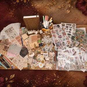 May include: A comprehensive stationery set featuring a brown hardcover journal, various colourful pens, numerous decorative sticker sheets with floral and vintage motifs, patterned paper scraps, washi tape rolls, and small ink pads arranged on a wooden surface.