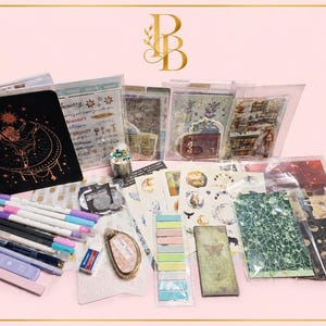 May include: A stationery set featuring a black notebook with a gold celestial dancer design, various sticker sheets, decorative paper, colourful markers, a glue tape dispenser, an eraser, and pastel sticky note tabs for journaling and scrapbooking.