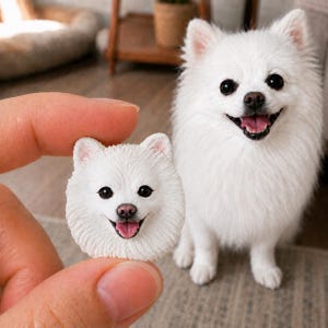 Könnte beinhalten: Eine kleine, weiße, skulptierte Hundekopffigur mit strukturiertem Fell, schwarzen Augen und einer rosa Zunge, die zwischen den Fingern gehalten wird, neben einem flauschigen weißen Hund mit ähnlichem Aussehen, schwarzen Augen und offenem Maul.