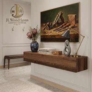 May include: A floating wooden console shelf with a dark brown finish, featuring a blue ceramic vase with flowers, a stack of three books, a small rectangular wooden box, a gray abstract sculpture, and a brass desk lamp with a conical shade.