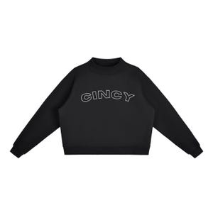 Puede incluir: Una sudadera negra de manga larga con cuello alto y puños acanalados. La palabra CINCY está impresa en el pecho con una tipografía blanca delineada. La prenda tiene un dobladillo recto y un color negro sólido en todo el diseño.