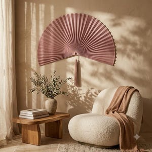 Dusty rose bamboo wall fan displayed above a low wooden bed in a bright boho bedroom with neutral bedding and natural decor.