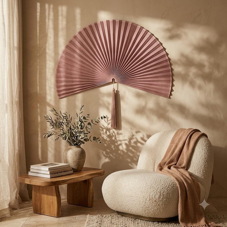 Dusty rose bamboo wall fan displayed above a low wooden bed in a bright boho bedroom with neutral bedding and natural decor.