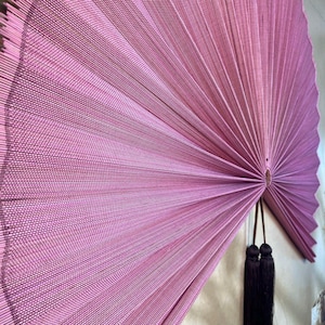 Close-up of a mauve pink bamboo wall fan showing intricate handwoven thread texture, finely arranged bamboo slats, radial folding pattern and detailed center knot.