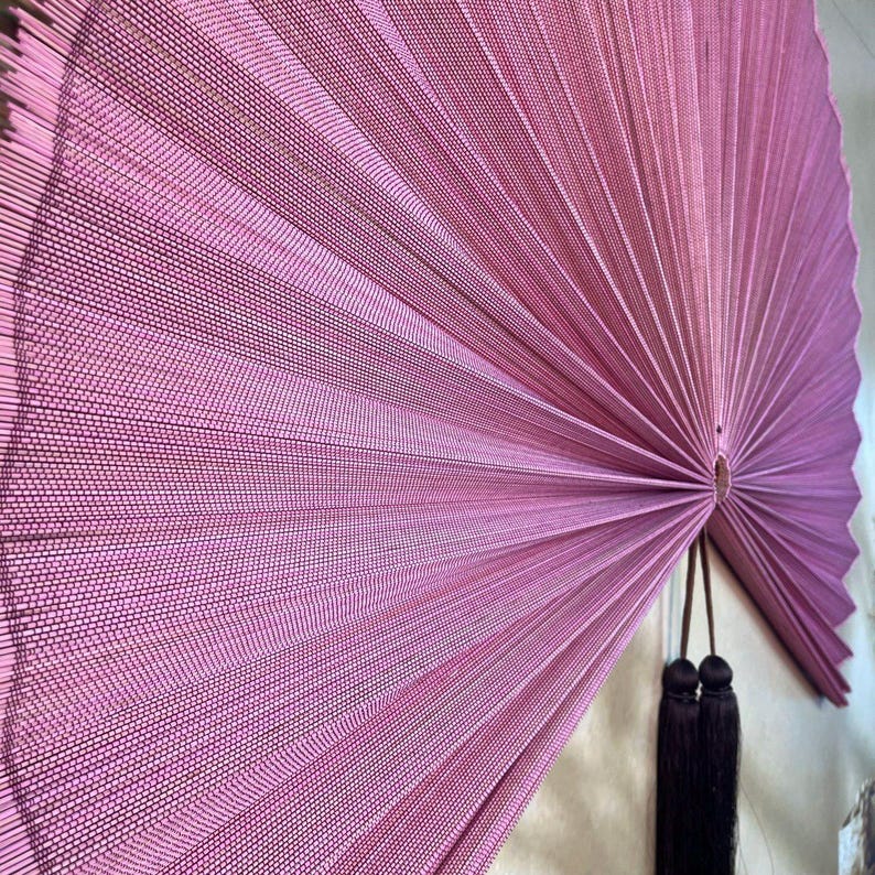 Close-up of a mauve pink bamboo wall fan showing intricate handwoven thread texture, finely arranged bamboo slats, radial folding pattern and detailed center knot.