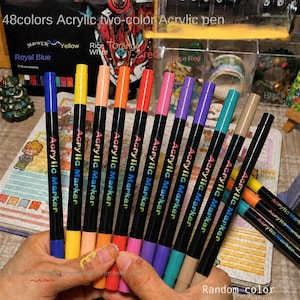 Puede incluir: Un conjunto de marcadores acrílicos con cuerpos negros y tapas de colores, cada uno etiquetado con el texto Acrylic Marker. Los bolígrafos presentan varios colores de tinta, incluyendo azul, amarillo, blanco, naranja, rojo, rosa, morado, turquesa y beige.
