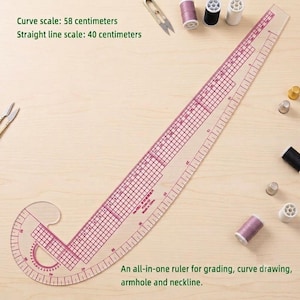May include: A clear plastic sewing ruler with red grid markings and measurements, featuring a curved edge for armholes and necklines. The ruler has a 58 centimeter curve scale and a 40 centimeter straight line scale, accompanied by sewing notions.