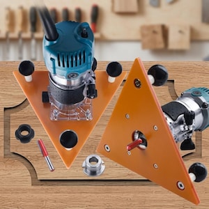 Op de afbeelding: Een blauwgroene en zilverkleurige elektrische bovenfrees met een driehoekige oranje grondplaat en drie zwarte knoppen. Het gereedschap bevat een freesbit met rode punt, een metalen kraag en een zwarte ronde moer voor houtbewerking.