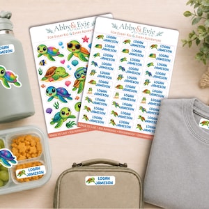May include: Two sheets of custom name stickers featuring green sea turtle illustrations and the text Logan Jameson, alongside a gray water bottle, a food container with grapes and crackers, a lunch bag, and a gray shirt, all labeled with the stickers.