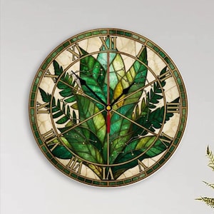May include: A round wall clock featuring a stained glass style design of green fern leaves. The clock face has a cream-colored background with black Roman numerals and thin black hour and minute hands, along with a thin red second hand.