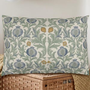 May include: A rectangular throw pillow featuring a repeating botanical pattern of blue pomegranates, sage green acanthus leaves, and small yellow flowers on a cream-colored background. The design is symmetrical with intricate, flowing foliage.