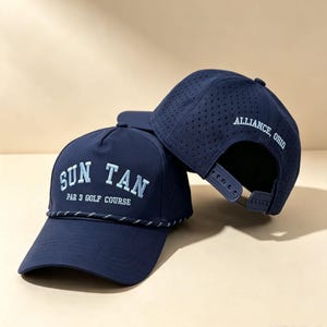 May include: A navy blue baseball cap with a perforated back panel and a snapback closure. The front features embroidered light blue text reading SUN TAN PAR 3 GOLF COURSE. A decorative rope trim sits above the brim. The side displays ALLIANCE, OHIO.