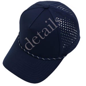 K&ouml;nnte beinhalten: Eine marineblaue Baseballkappe mit einer festen Vorderseite und einem perforierten Netzr&uuml;cken zur Bel&uuml;ftung. Eine d&uuml;nne, gedrehte wei&szlig;-marineblaue Kordel verl&auml;uft &uuml;ber der Basis der Krone, direkt &uuml;ber dem gebogenen Schirm. Das Wort details ist sichtbar.
