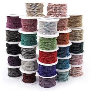 Könnte beinhalten: Eine Sammlung mehrerer Spulen mit Strasskettenbesatz in verschiedenen Farben, darunter Rot, Blau, Grün, Lila, Silber, Gold und Schwarz. Jede Spule enthält einen durchgehenden Strang aus kleinen, facettierten Kristallen auf einer Metallbasis.