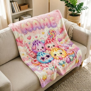 Puede incluir: Una manta de felpa suave con un fondo degradado en rosa y morado pastel con la palabra NAME impresa en letras grandes y redondeadas. El diseño incluye dibujos animados de dumplings, una piruleta, un boba, corazones, estrellas y dulces.