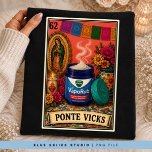 May include: A black fabric item featuring a graphic print of a Vicks VapoRub jar, a candle, flowers, and a religious icon. The design includes the text 62 and PONTE VICKS, with colorful papel picado banners hanging across the top of the illustration.