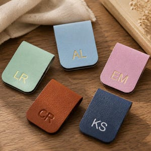 Può includere: Cinque segnalibri magnetici rettangolari in azzurro, verde menta, rosa, marrone e blu scuro. Ogni segnalibro presenta due lettere maiuscole impresse in oro o bianco, nello specifico AL, LR, EM, CR e KS, con una finitura liscia e testurizzata.