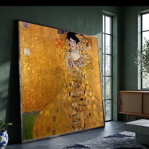 Puede incluir: Una gran impresión de arte mural rectangular enmarcada que presenta el retrato de una persona con cabello oscuro sobre un fondo dorado vibrante. La obra muestra patrones geométricos complejos, motivos de ojos y detalles en pan de oro.
