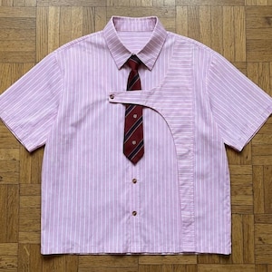 Peut inclure: Une chemise à manches courtes avec un motif à rayures verticales rose clair et blanc. La chemise présente un empiècement asymétrique sur le devant et une cravate rouge foncé avec de fines rayures diagonales bleues et blanches attachée.