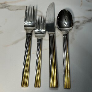 May include: A four-piece stainless steel flatware set consisting of a large fork, a smaller fork, a dinner knife, and a spoon. Each utensil features a polished silver-tone head and a handle with a decorative, diagonal twisted pattern.