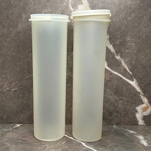 May include: Two tall, cylindrical, translucent off-white plastic storage containers. One container is open at the top, while the other is capped with a matching circular lid. These slender, vertical vessels feature a smooth, matte finish.