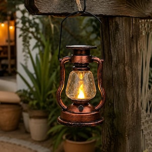 May include: A rustic, copper-coloured metal lantern with a clear glass globe and a black wire handle. The lantern features a solar-powered light source inside that emits a warm, flickering glow, suspended from a wooden beam by a thick rope.