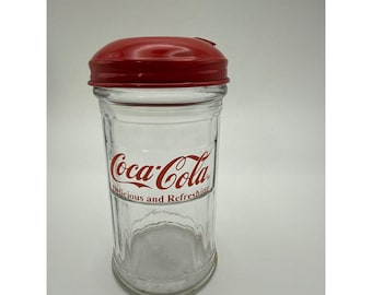 Azucarero de vidrio Coca-Cola vintage de 1995 con tapa metálica roja abatible, estilo retro de restaurante.
