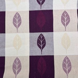 May include: A woven fabric featuring a repeating grid pattern of alternating squares in deep purple, light beige, and grey. Each square contains a single leaf motif with a central vein and lateral veins, rendered in a contrasting color to the square.