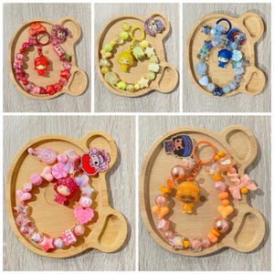 May include: Five circular beaded keychains featuring colorful plastic beads in red, yellow, blue, pink, and orange. Each keychain includes a central character charm, various shaped beads like stars and hearts, and a metal ring for attachment.