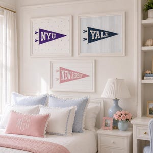 Op de afbeelding: Drie ingelijste wandkunstwerken met wimpels met de tekst NYU, YALE en NEW JERSEY. De NYU-print heeft een witte achtergrond met stippen, de YALE-print heeft blauwe verticale strepen en de NEW JERSEY-print heeft een witte achtergrond met planken.