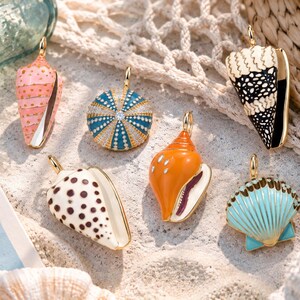 May include: Six gold-toned metal pendants shaped like seashells and a sea urchin, featuring colorful enamel details in pink, teal, orange, black, and white. Each charm includes a small loop for hanging, with some pieces displaying intricate patterns.