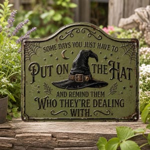 Può includere: Una targa rettangolare in metallo verde oliva con angoli superiori arrotondati, raffigurante un cappello da strega nero e il testo: SOME DAYS YOU JUST HAVE TO PUT ON THE HAT AND REMIND THEM WHO THEY'RE DEALING WITH. Decorata con motivi a ragnatela.