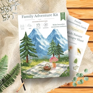 May include: A Family Adventure Kit outdoor activity pack featuring a mountain landscape illustration with pine trees, a picnic basket on a checkered blanket, and text including Family Adventure Kit, Outdoor Activity Pack, and Gather&Wander Co.