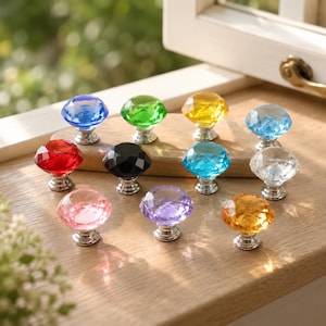 May include: A collection of eleven faceted, diamond-shaped cabinet knobs in various colours including blue, green, yellow, light blue, red, black, clear, pink, purple, and orange, each featuring a polished silver-toned metal base.