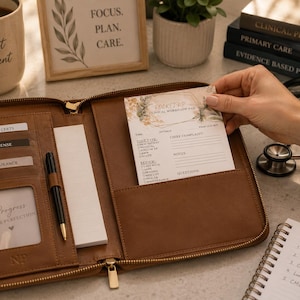 Pode incluir: Uma pasta organizadora de couro castanho com fecho, contendo ranhuras para cartões etiquetadas como CME & CERTS, LICENSE e INSURANCE, um suporte para caneta com uma caneta preta e um bloco de notas. Um bloco de fluxo clínico com flores está no bolso.