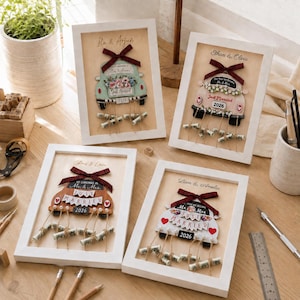 May include: Four white framed shadow boxes featuring personalized wedding car illustrations with names, the text Just Married, and the year 2026. Each car is adorned with a plaid ribbon and attached to small rolled paper scrolls hanging by twine.