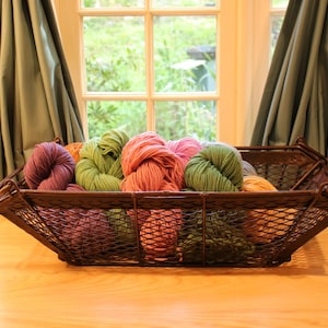 May include: A rectangular dark brown metal wire basket filled with multiple skeins of yarn in various colours including purple, light green, coral pink, and orange. The basket features a diamond-shaped mesh pattern and two side handles.