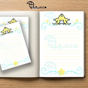 May include: A notebook with an open page featuring a yellow star-shaped character, light blue swirling lines, and umbrella icons. A smaller matching stationery sheet overlaps the notebook. A blue pen lies to the left. The text Riniwaco is visible.