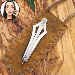 May include: A silver-colored metal jaw harp with a central trigger, resting on a brown leather pouch featuring laced edges and a leather cord. An inset illustration shows a person playing the instrument by placing it against their lips.