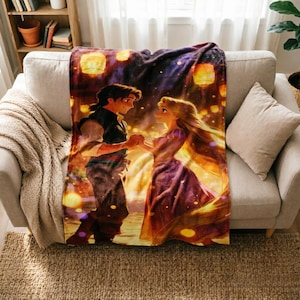 Puede incluir: Una manta de forro polar suave que presenta una ilustración colorida de los dos personajes de la película Enredados, Rapunzel y Flynn Rider, bailando juntos bajo un cielo nocturno lleno de linternas flotantes brillantes en tonos dorados y naranjas.